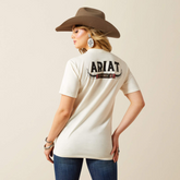 Woman wearing a cream-colored Ariat shirt and brown cowboy hat on a beige background